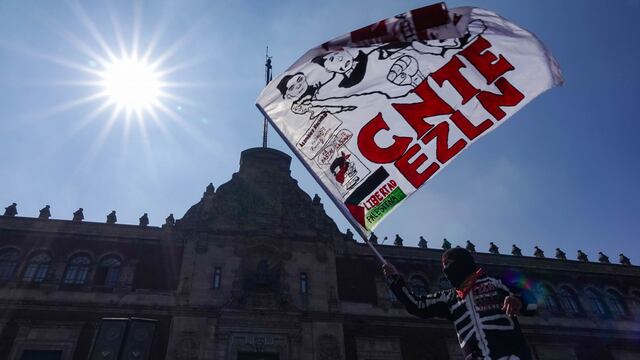Un hombre caracterizado con pasamontañas del EZLN ondea una bandera de la CNTE en la plancha del Zócalo