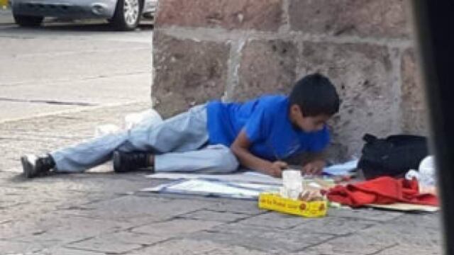 Niño vende dulces y hace tarea en la calle
