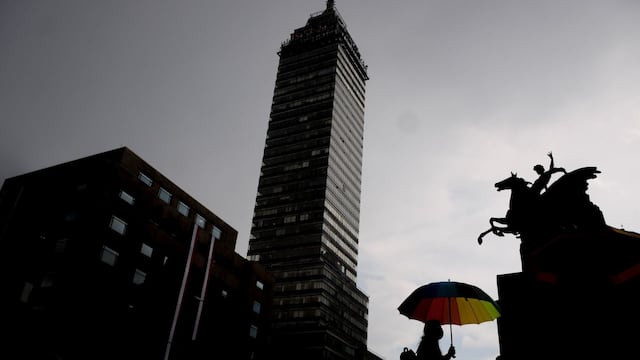 Una joven camina por la explanada de Bellas Artes mientras se protege de la lluvia