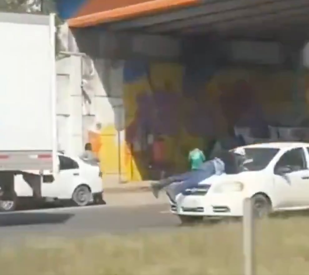 Hombre sobre el cofre de un automóvil en movimiento