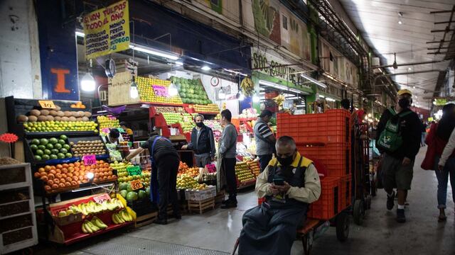 Un diablero espera mirando su celular a un costado de un puesto de frutas en la Central de Abastos