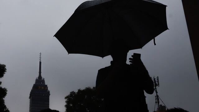 Una persona observa su celular mientras camina utilizando un paraguas para protegerse de la lluvia