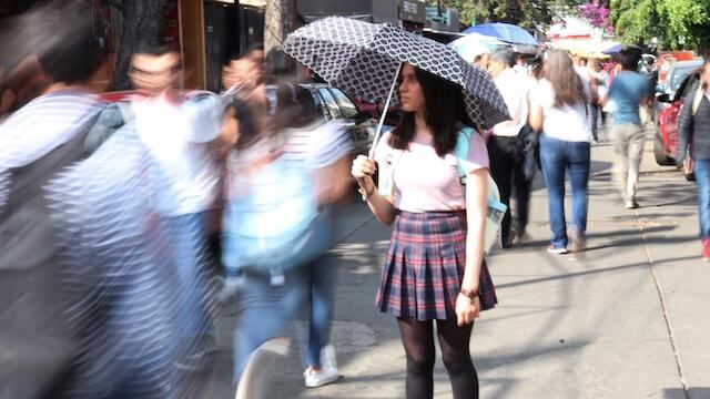 Una joven usa sombrilla para cubrirse del rayo del sol.