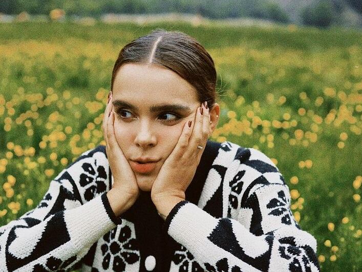 Yuya sentada en un campo con flores.