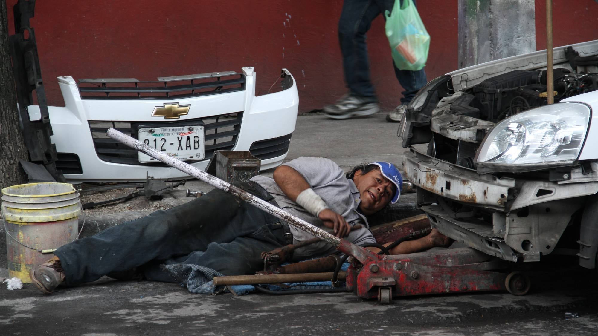 Un mecánico ejerce su profesión en la vía pública. Casi 6 de cada 10 trabajadores en México no cuentan con seguridad social.