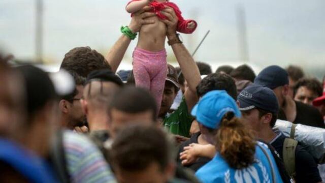 Un hombre sostiene un niño por encima de decenas de migrantes y refugiados que esperan para subir a un tren.