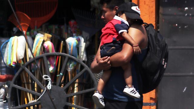 Un hombre camina por una calle de Cuernavaca cargando a su hijo