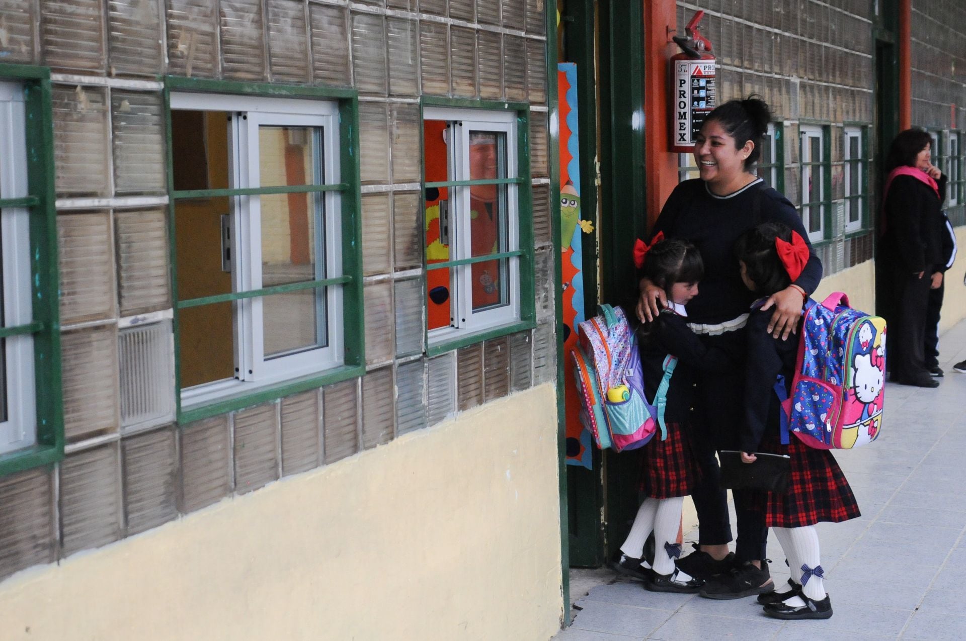 Maestra saluda a dos alumnas a la entrada de su salón de clases