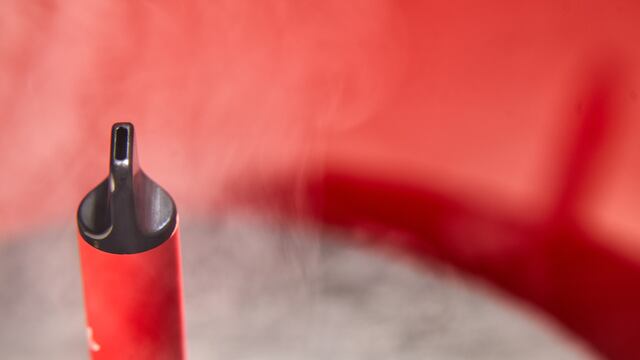 One disposable red e-cigarettes, and vapes in with smoke. Concept of bad habits, modern smoking electronic cigarettes. Copy space.