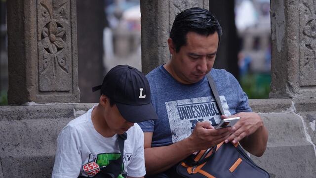 Un niño acompañado de su padre observan su celular en la Alameda Central