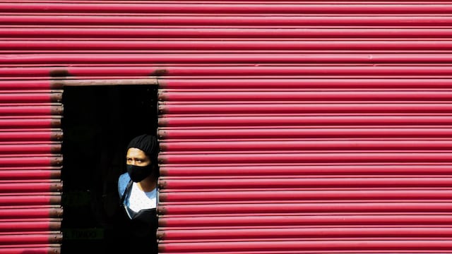 Una mujer se asoma por la puerta de su negocio antes de abrirlo durante esta mañana de lunes