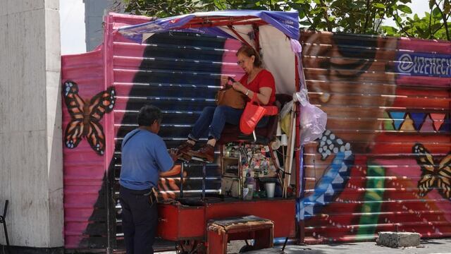 Un lustrador cepilla un zapato mientras una mujer observa su celular en Avenida Reforma