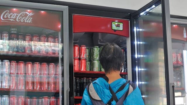Una mujer adquiere una bebida saborizada en una tienda de conveniencia.