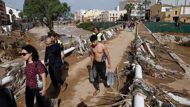 Varias personas transportan agua potable por uno de los puentes que cruza el barranco de Paiporta, Valencia,