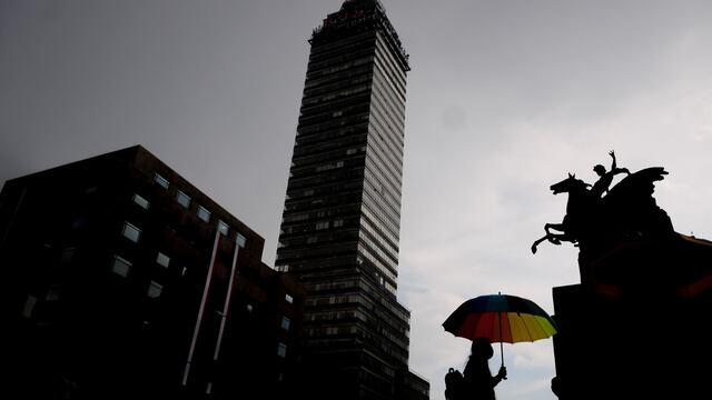 Una joven camina por la explanada de Bellas Artes mientras se protege de la lluvia