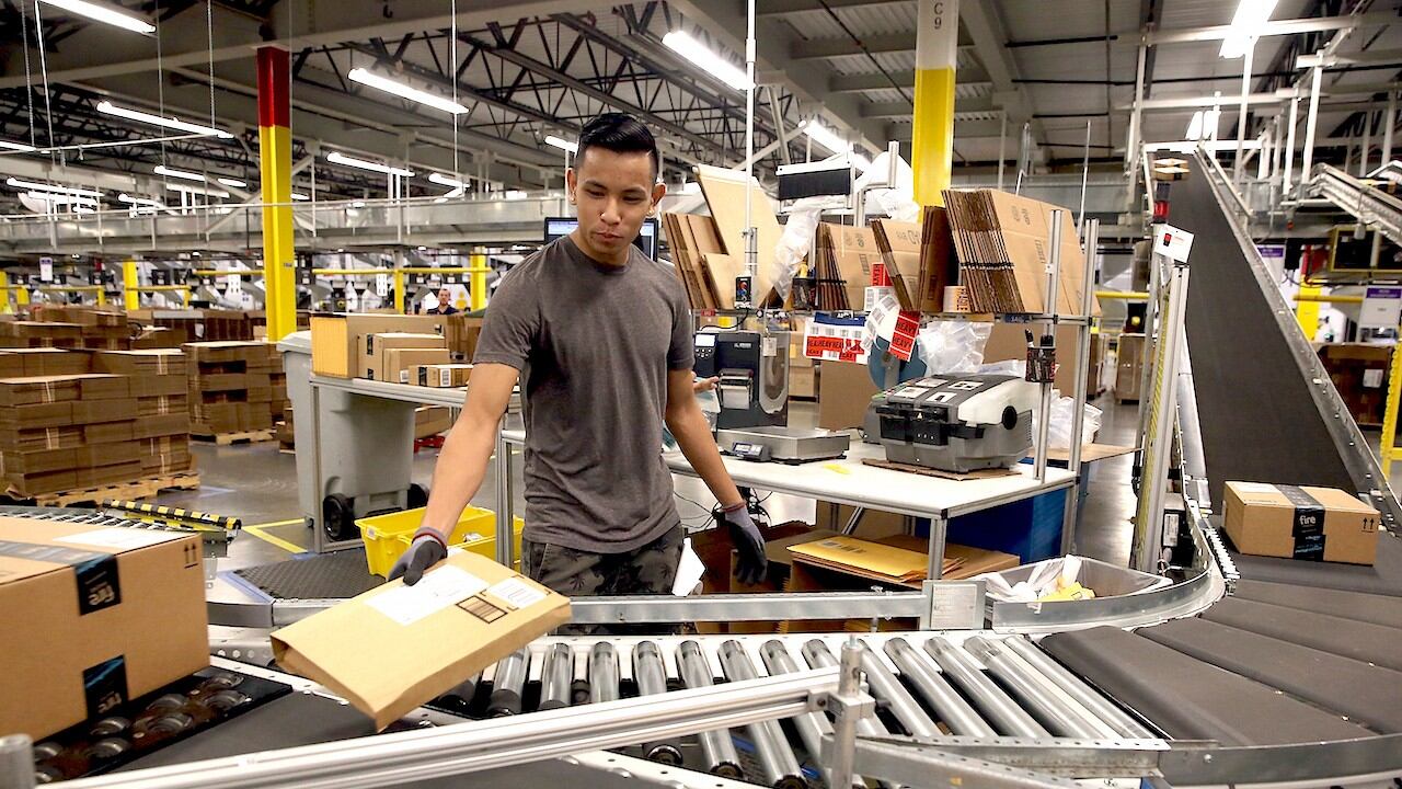 Trabajador de Amazon clasificando paquetes en una cinta transportadora.