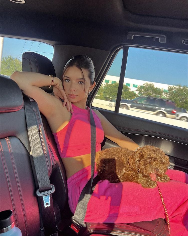 Ángela Aguilar posa con un conjunto rosa y su perro sobre sus piernas.