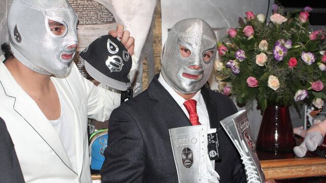 Hijo del Santo y Santo Jr. posan con artículos promocionales.