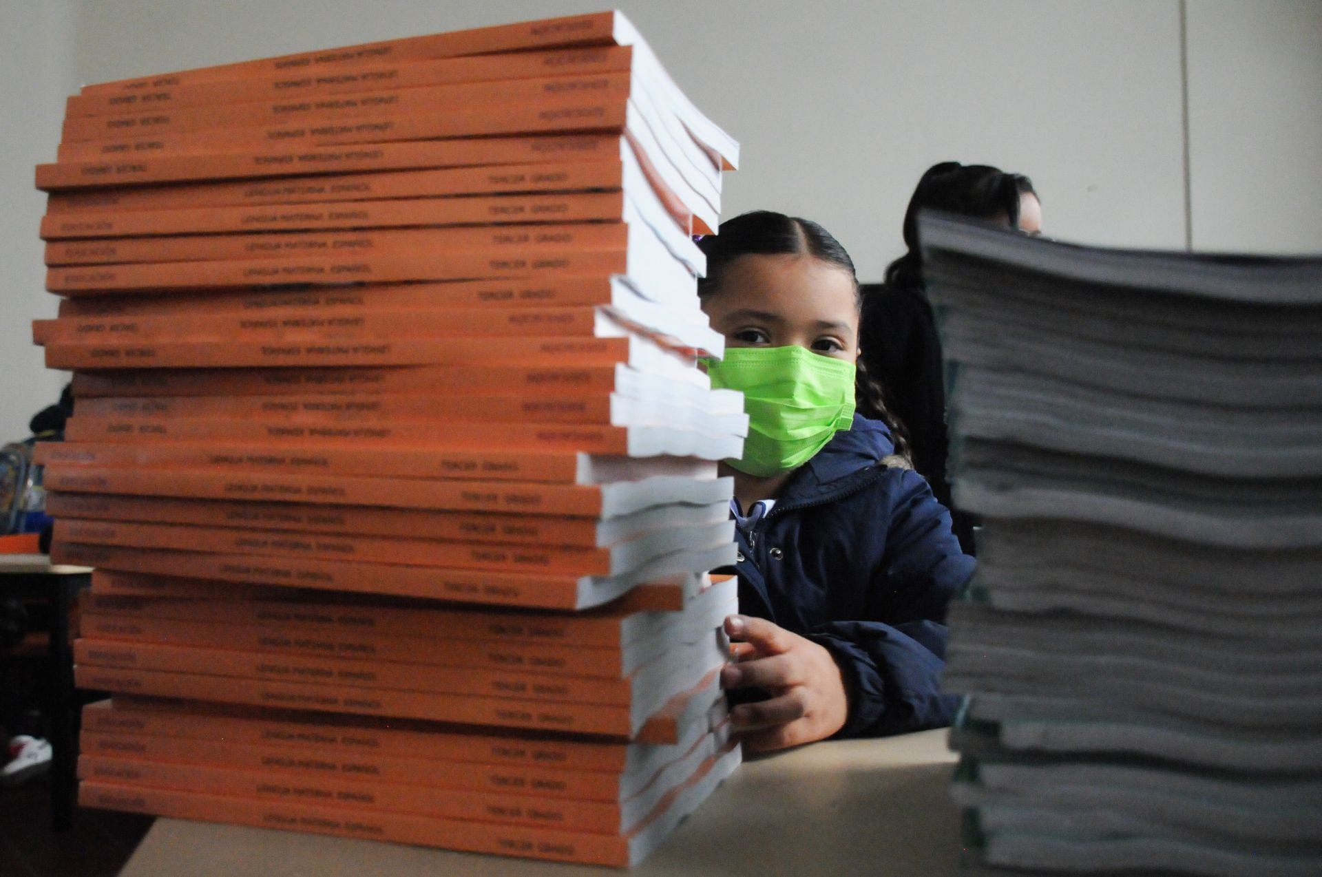 Una niña se asoma detrás de los nuevos libros de texto de la SEP
