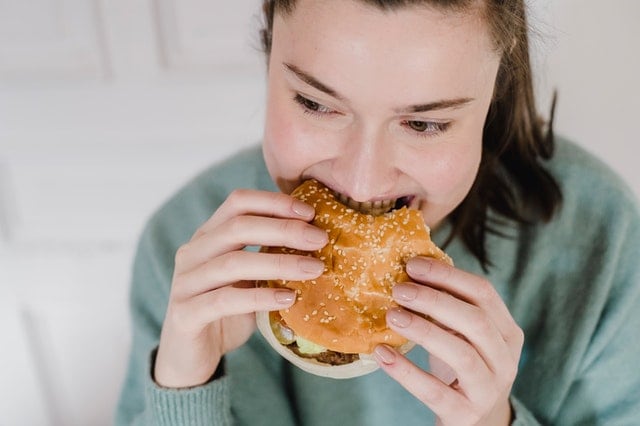 Mujer mordiendo hamburguesa.