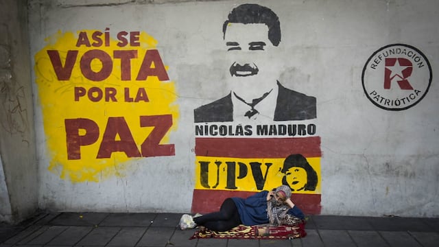 Una mujer en situación de calle está recostada frente al centro de votación Andrés Bello. Tras ella, la propaganda oficial del actual presidente y candidato, Nicolás Maduro