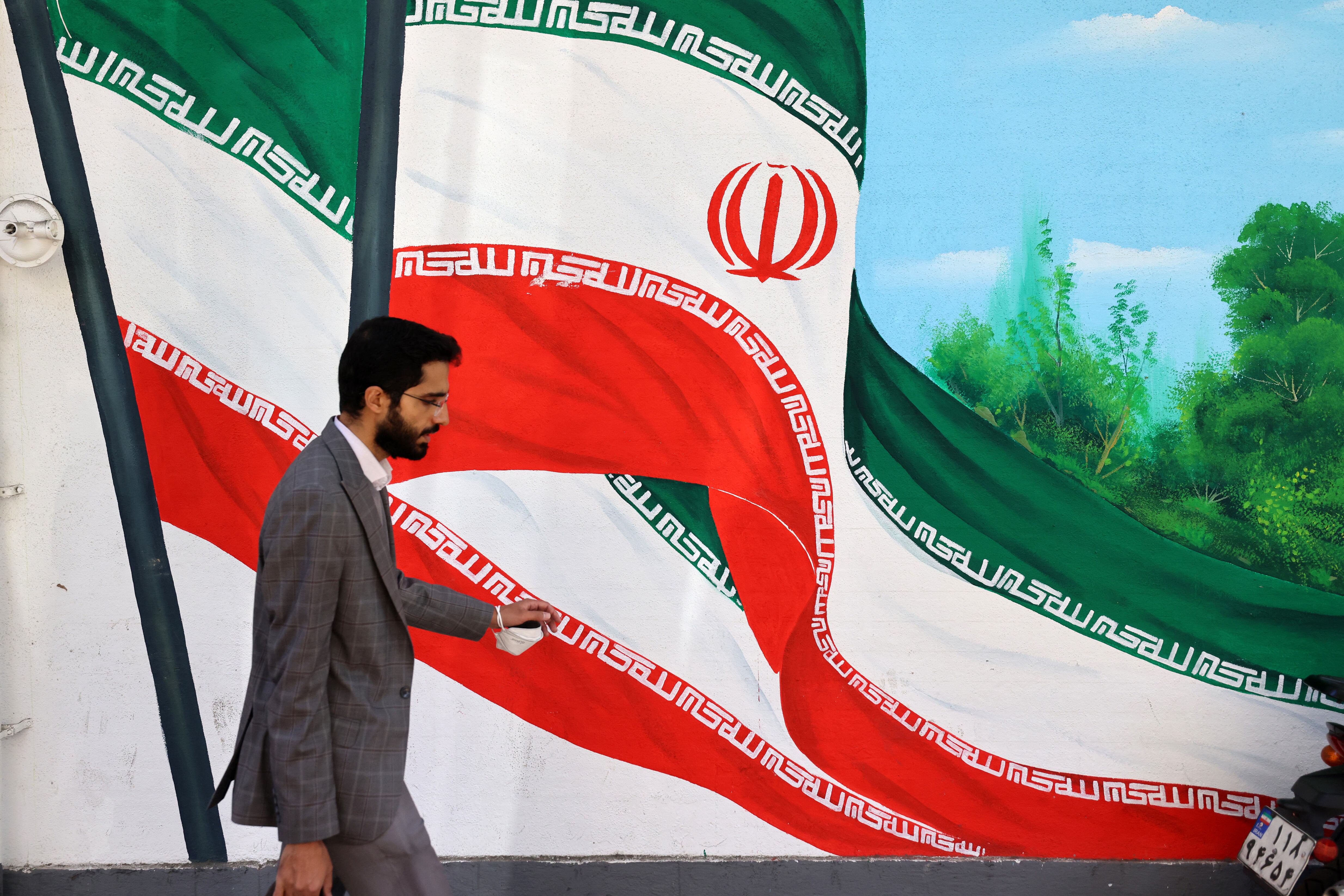 Hombre camina frente a un mural con la bandera de Irán